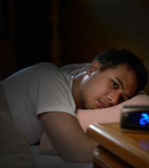 Depressed man suffering from insomnia lying in bed