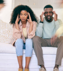 Tired parents on sofa with motion blur of energy as children run around house